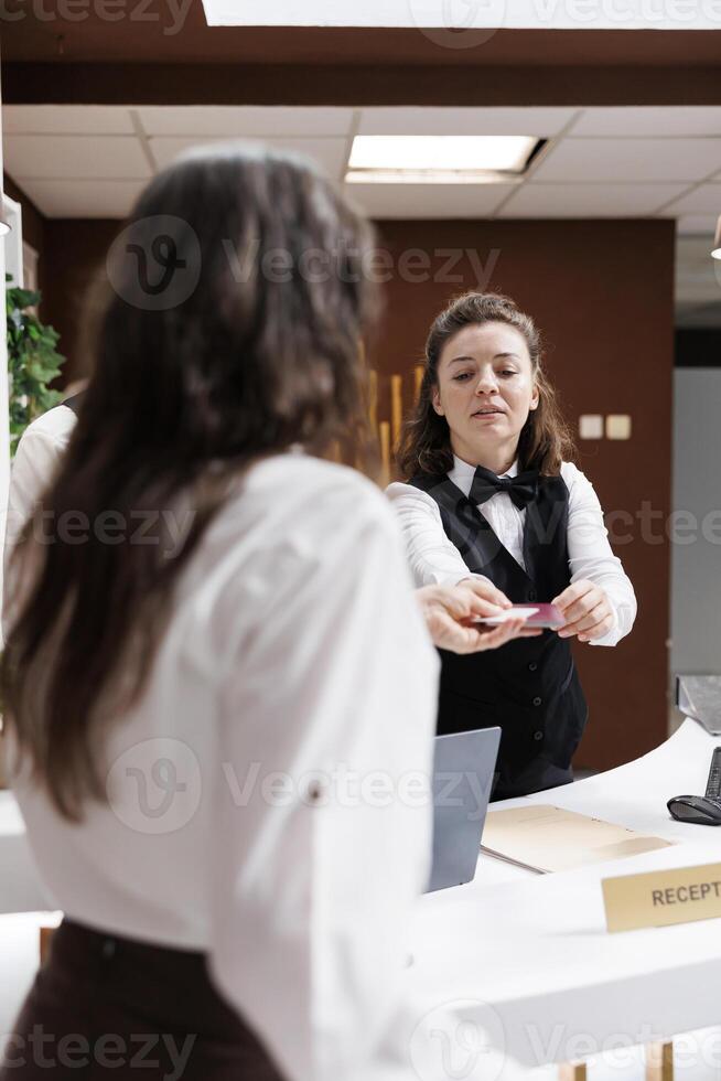 At hotel lobby counter, elderly female traveler checks in with passport. After establishing identity, kind concierge at registration counter returns the personal paperwork of retired senior woman. photo