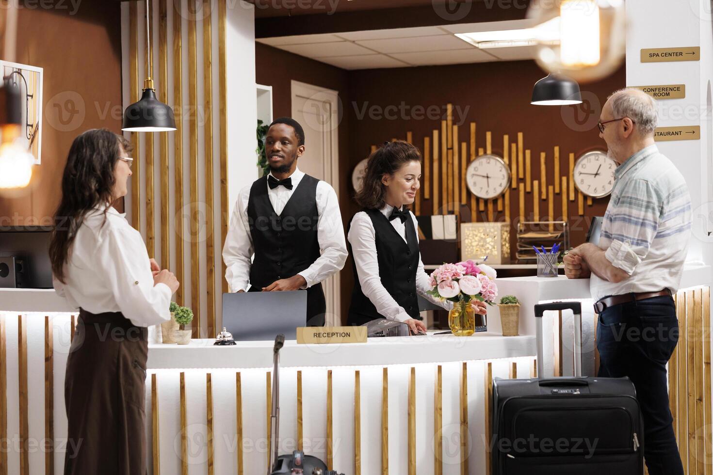 Employees assisting elderly male and female travelers at registration counter of hotel reception. Multiethnic receptionists welcoming senior visitors, providing helpful information for check-in. photo
