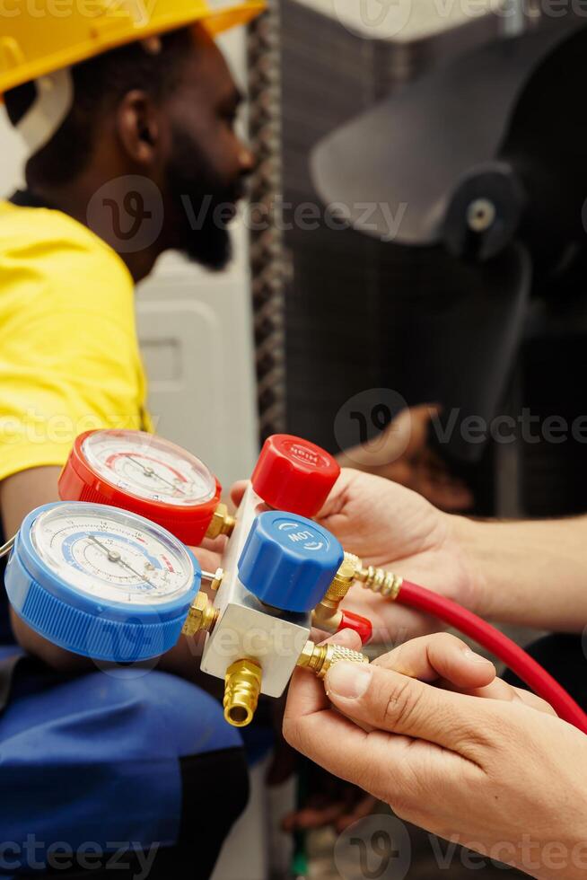 Capable electrician eliminating layer of dirt and dust from hvac system clogged air filters while coworker uses measurement device to check for freon leaks and read pressure in air conditioner system photo