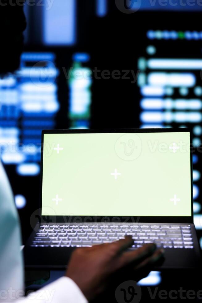 Close up shot of specialist examining server cabinets performance trends using chroma key device. Employee using mock up laptop to spot data center operational issues causing servers to malfunction photo