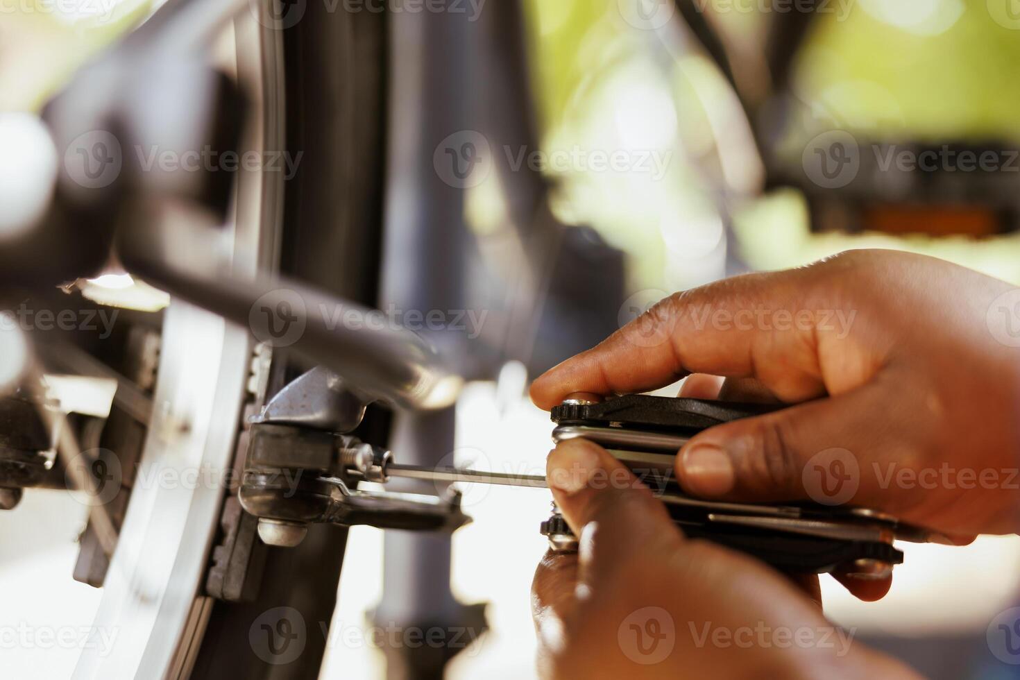 African american pair of hands gripping specialized equipment for adjusting and tightening bicycle hub and axle. Close-up shot of person grasping adjustable multitool for bike maintenance. photo