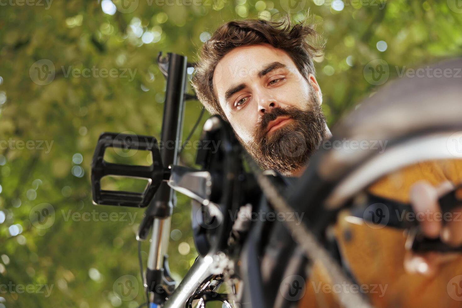 Active caucasian male working on broken bike wheel chain ring with professional equipment in home yard. Committed sporty man servicing bicycle outside for summer leisure cycling. photo