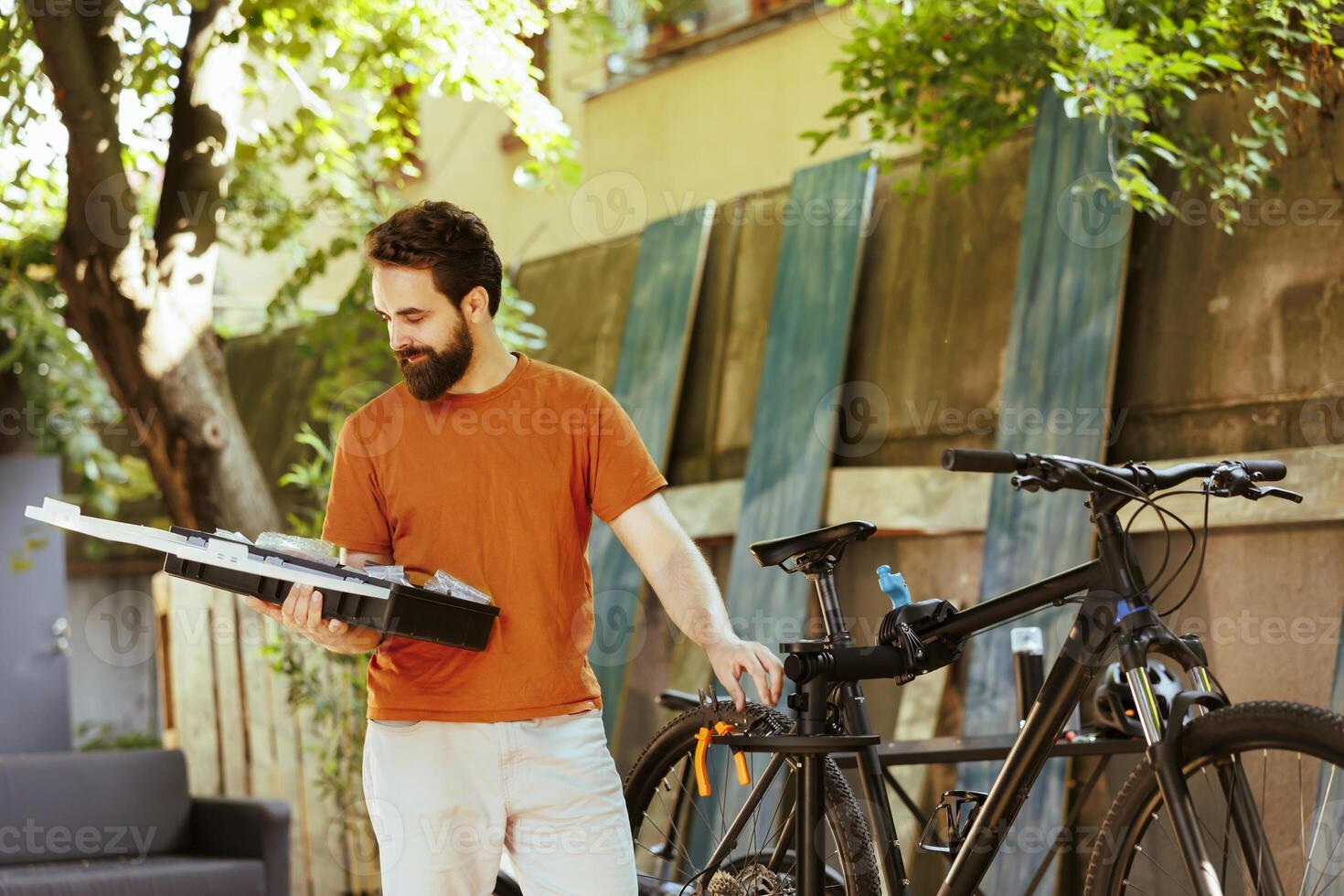 Image showing healthy athletic caucasian man holding his toolbox in home yard for bicycle maintenance. Sports-loving active male cyclist exploring professional equipments outside. photo