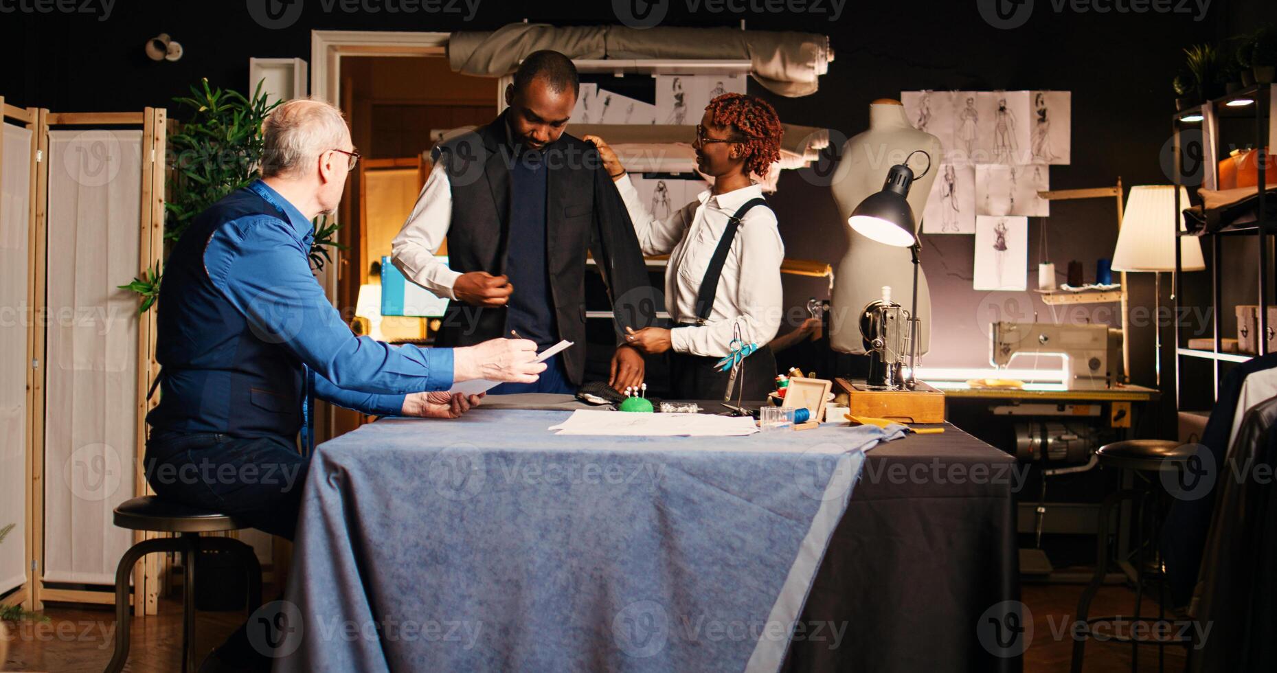 Atelier client trying on jacket to create custom made suit from experienced couturier, making sure about measurements. Senior tailor and woman manufacturing tailored blazer in workshop. photo