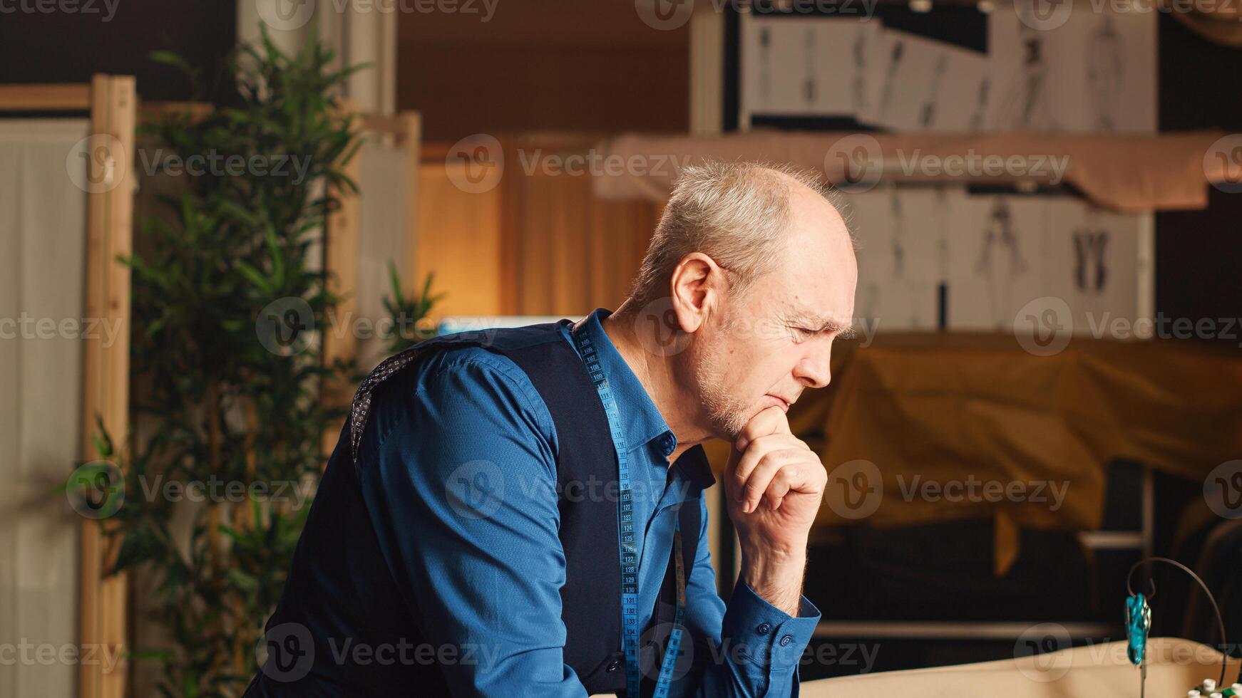 Tailor feeling stressed in workshop while he makes custom made luxury clothes, aiming for perfection in atelier. Business owner working in tailoring industry, frustrated under pressure. photo