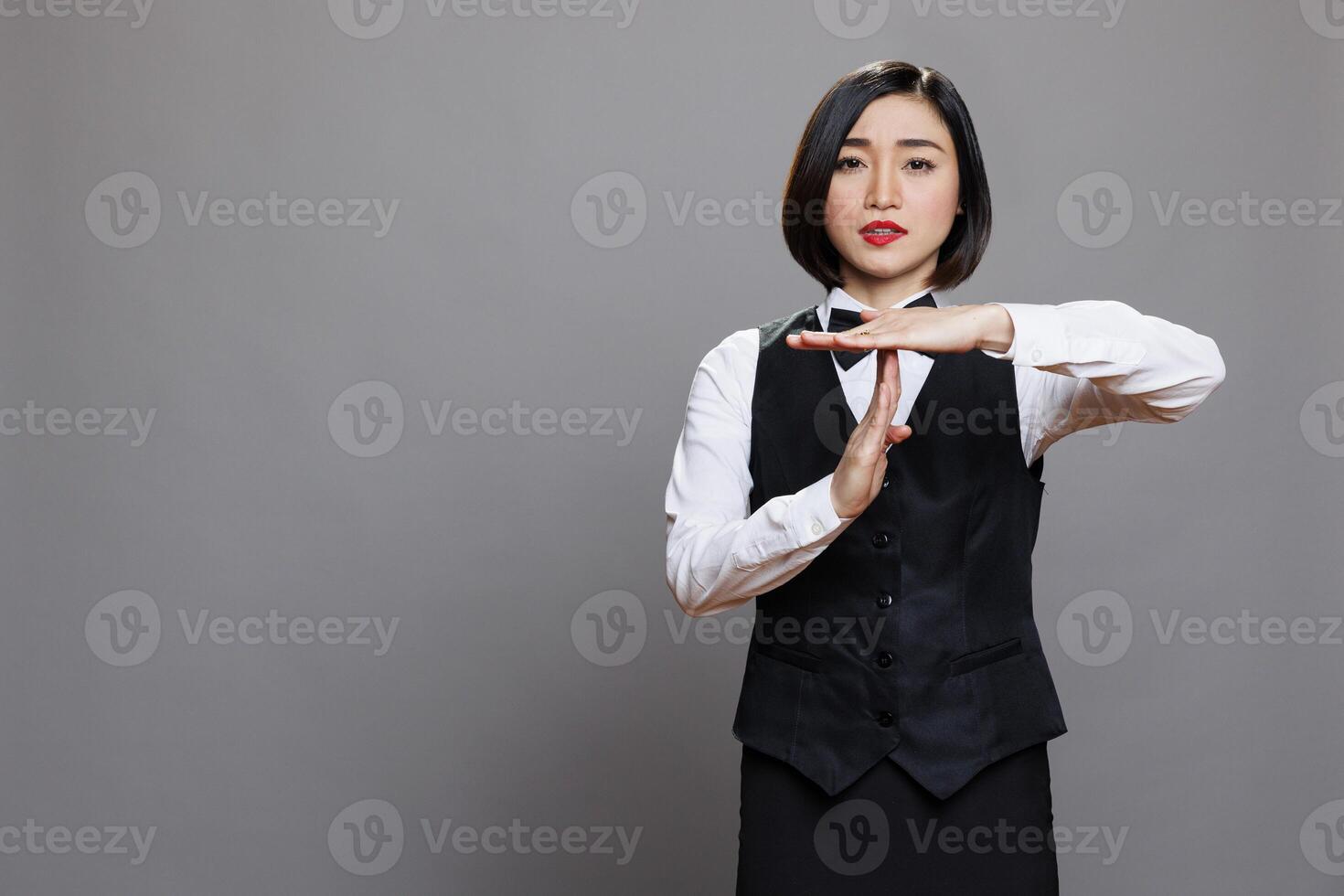 Serious asian waitress showing time out gesture with hands and looking at camera with confident facial expression. Young attractive woman receptionist making interruption symbol portrait photo