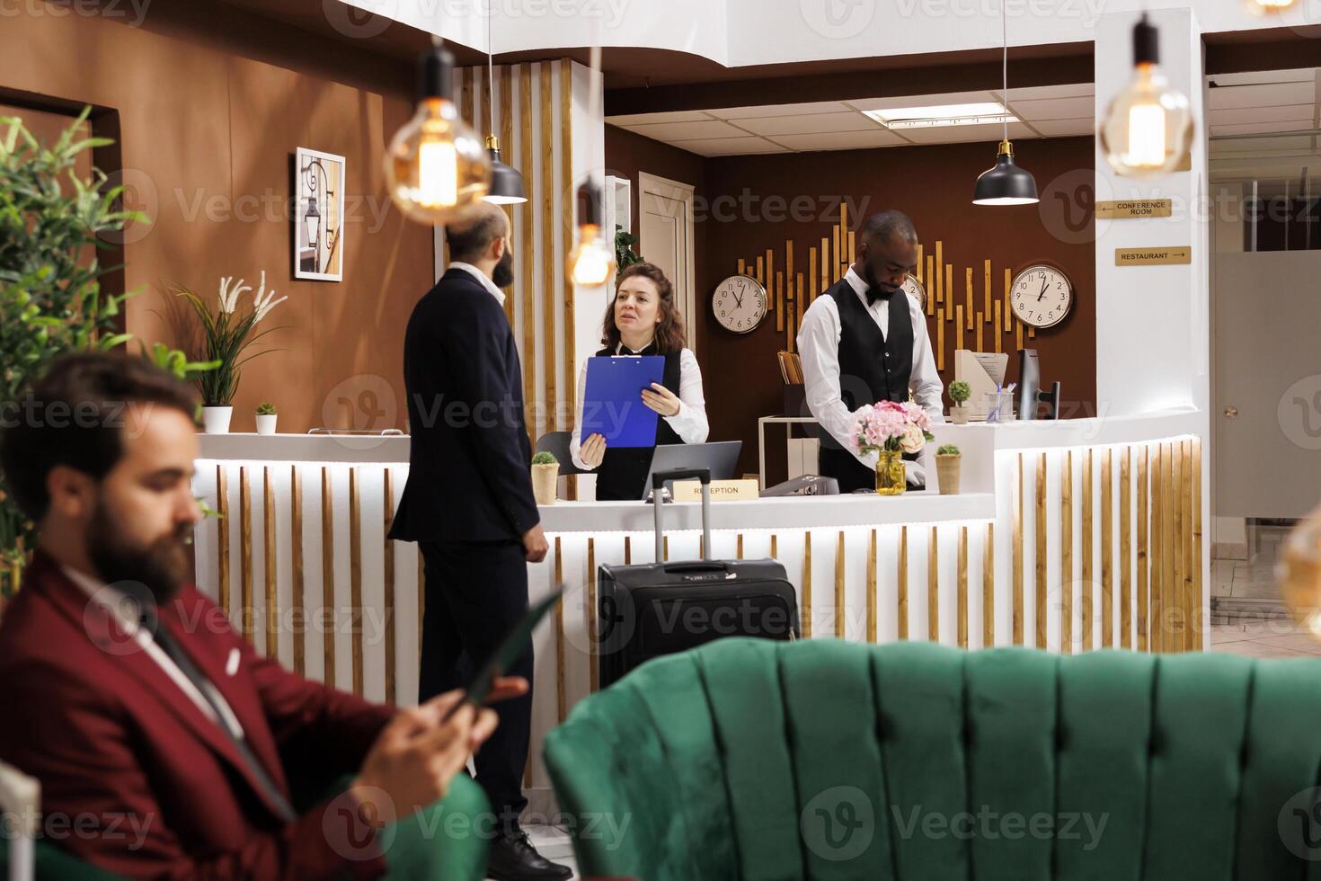 Man filling in reservation documents, approaching front desk reception with luggage in lobby. Businessman receiving good recommendations from hotel staff, travelling for work purposes. photo
