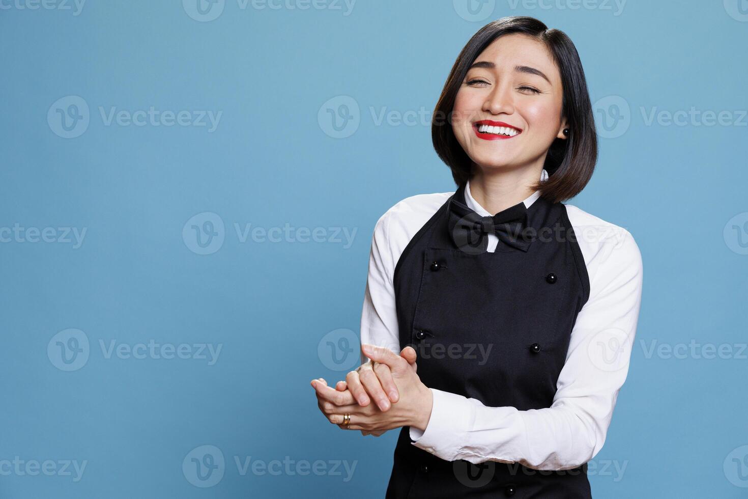 Smiling cafe waitress applauding with joy and encouragement, showcasing appreciation portrait. Attractive woman receptionist clapping hands and laughing while posing in studio photo