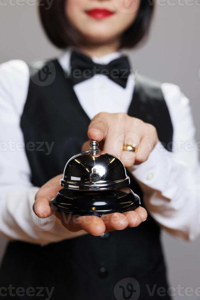 Waitress wearing professional uniform pressing hospitality bell with finger closeup. Restaurant woman receptionist holding dining alert, ringing and signaling about order photo