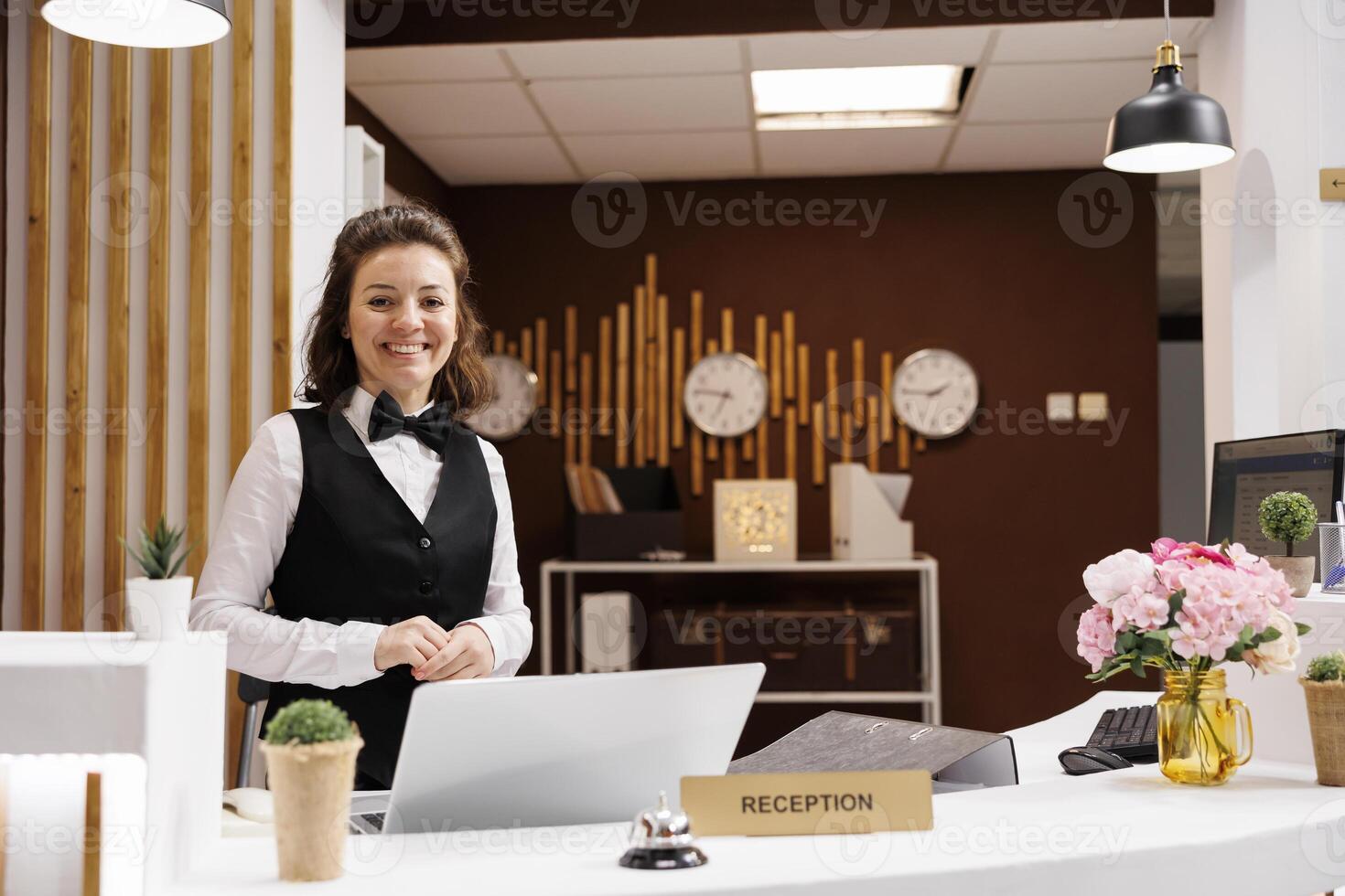 Front desk staff smiling at reception, welcoming hotel guests and providing luxury room services. Receptionist in formalwear being friendly, works on online bookings and reservations. photo
