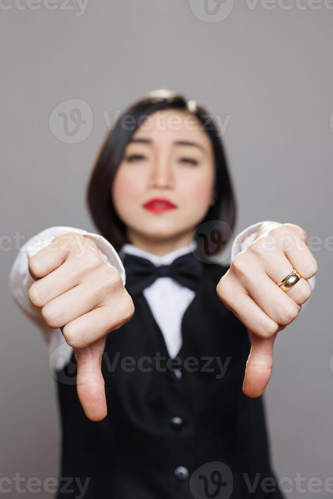 Asian waitress in uniform showing thumbs down gesture with closeup on hands. Cafe worker sharing restaurant negative experience and bad service feedback while looking at camera photo
