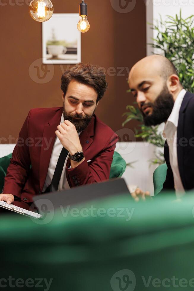 Employees in suits meet at hotel, discussing about new international partnership and sharing strategy ideas for common growth. Businessmen reviewing notes for conference with executive board. photo