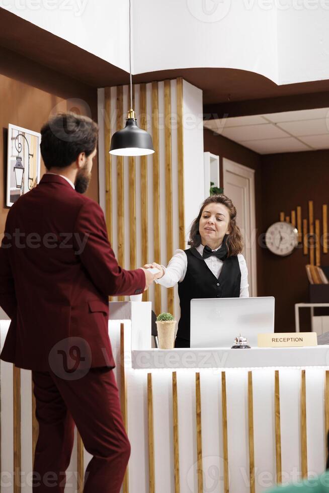 Front desk staff hands out access card for businessman, ensuring comfortable and hassle free stay at luxury hotel. Receptionist with impeccable customer service providing room key after long trip. photo