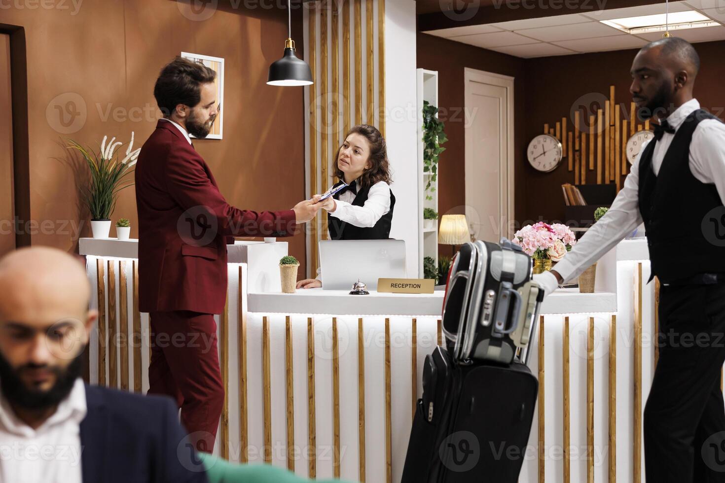 Formal guest fill in registration forms at front desk, doing easy check in process to see room reservation. Businessman travelling for work, receiving great concierge service from staff. photo