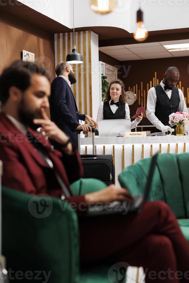 Passport id check in, businessman registering at hotel reception counter with professional employees. Entrepreneur talking to receptionist, reviewing identification documents. photo