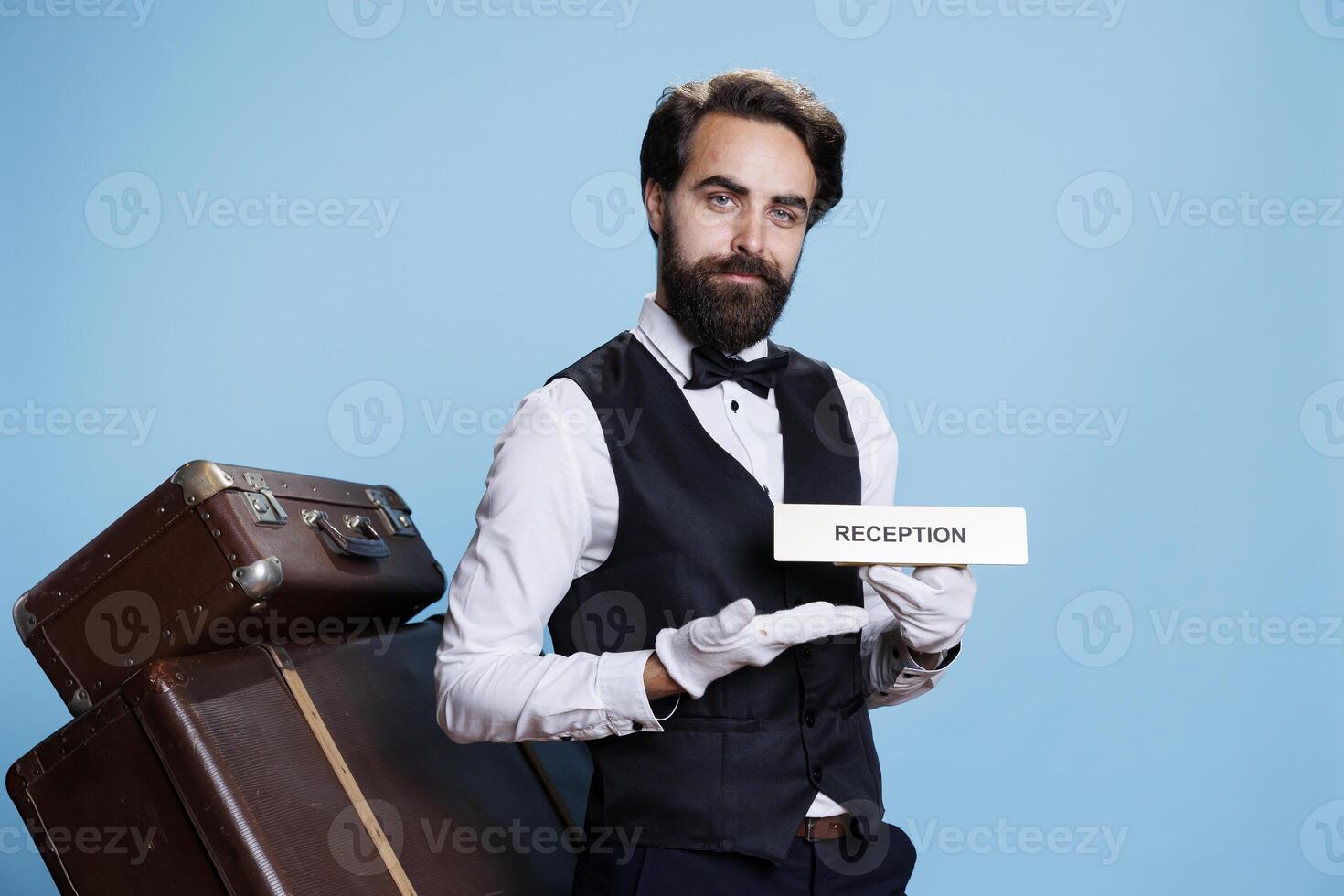 Doorman poses with sign of reception that guides persons to the hotel lobby area. Experienced staff member in the tourism industry using the entrance front desk symbol indicator. photo