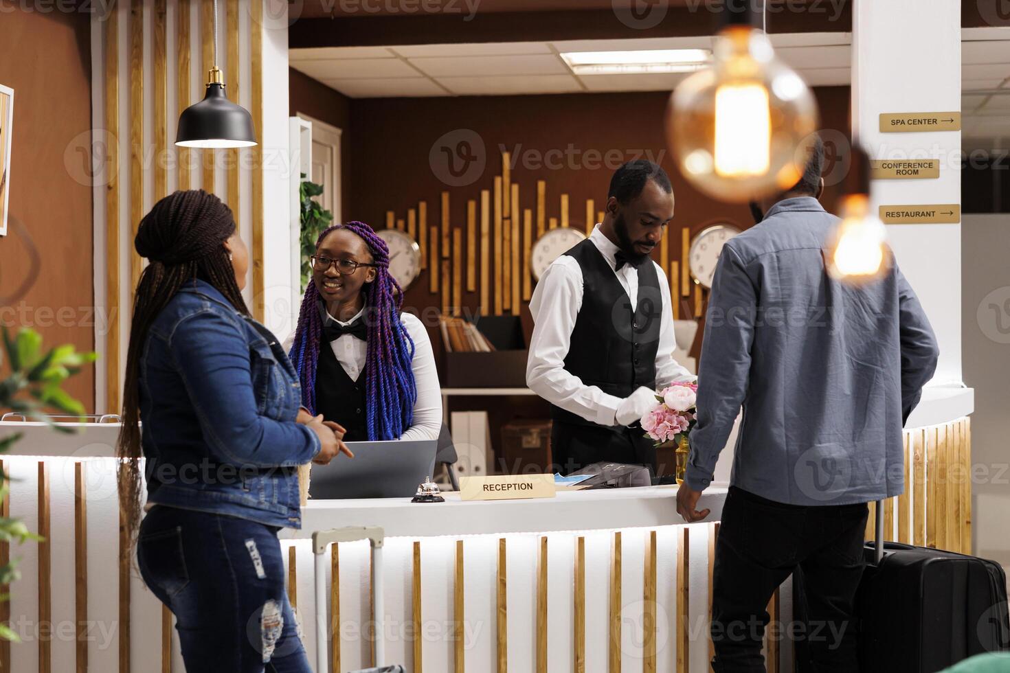 Friendly smiling front desk staff welcoming visitors at reception area of hotel. Smiling African American receptionist giving arriving guests information. People checking in at resort photo