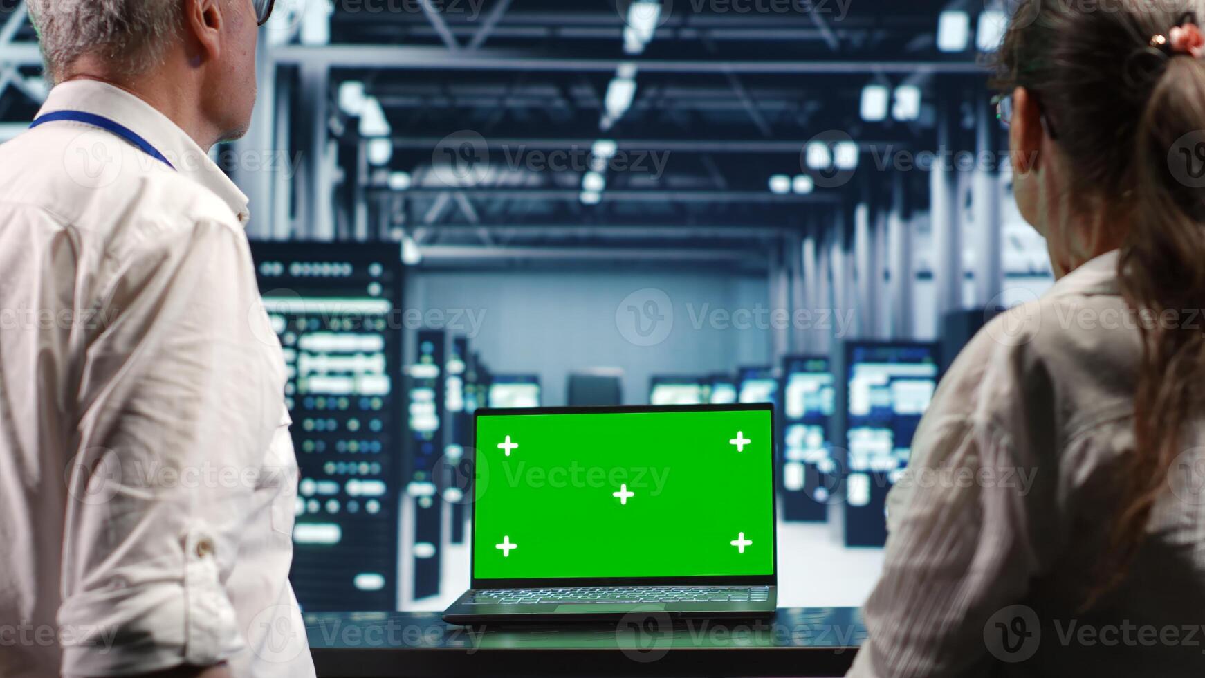 System administrators looking around high tech data center, using mockup laptop to crosscheck disaster recovery plan and assess server hardware in need of replacement, preventing disruption photo