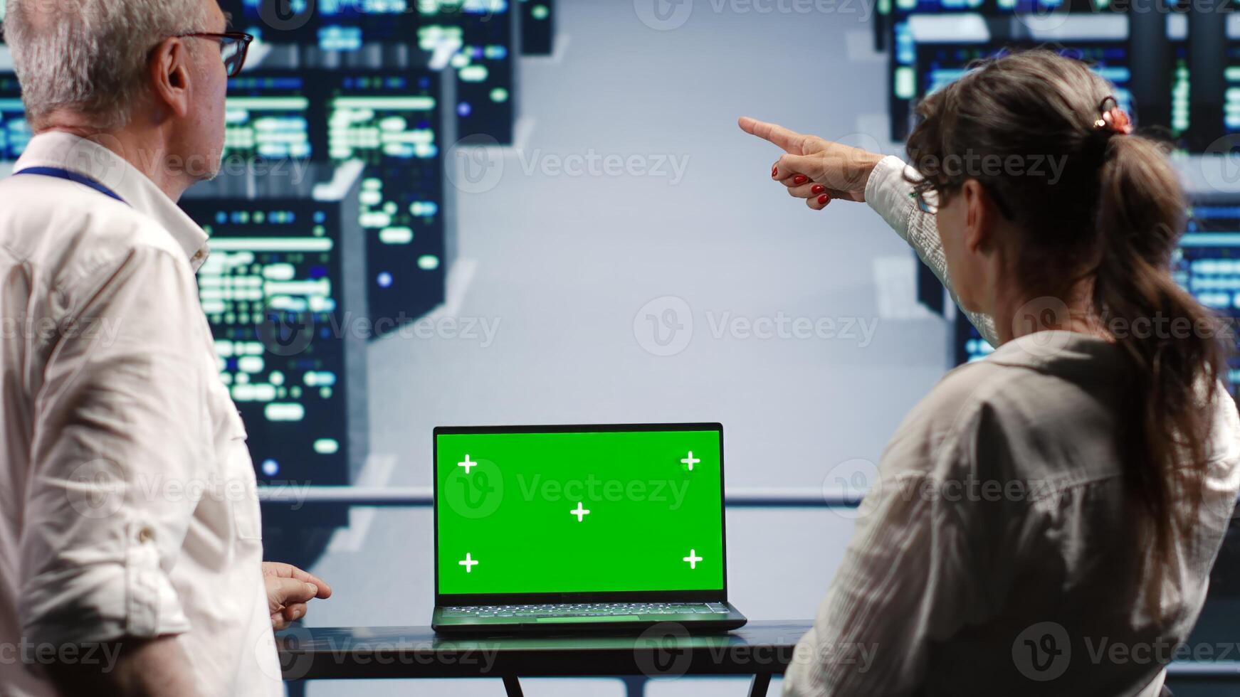 Coworkers in server farm housing high end processors capable of quickly and efficiently performing complex computations and data analysis, using green screen laptop to fix malfunctions photo