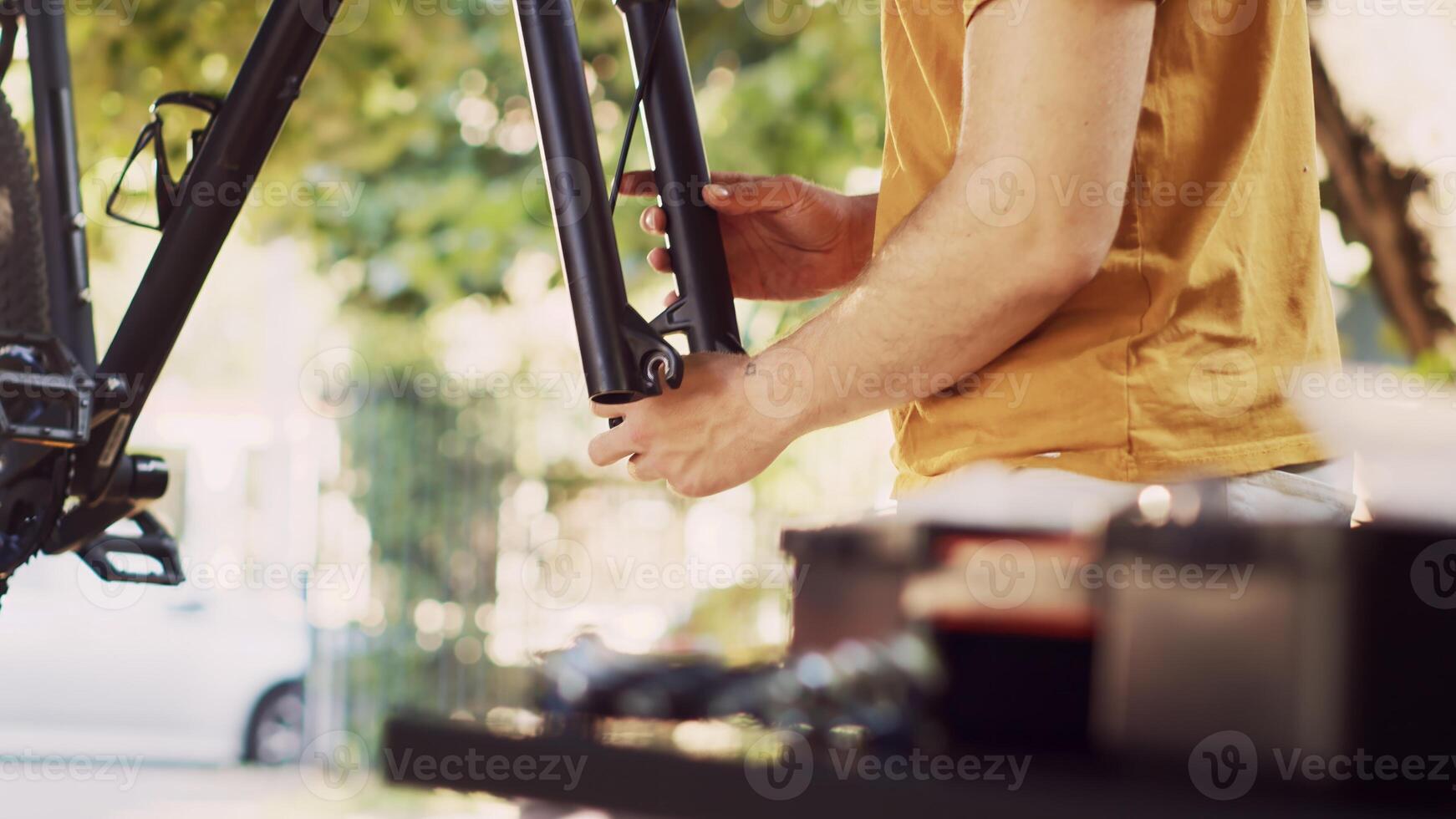 Young active man delicately detaching wheel and fine-tuning bike front fork and headset for safe outdoor cycling. Close-up of male cyclist repairing and adjusting broken modern bicycle. photo