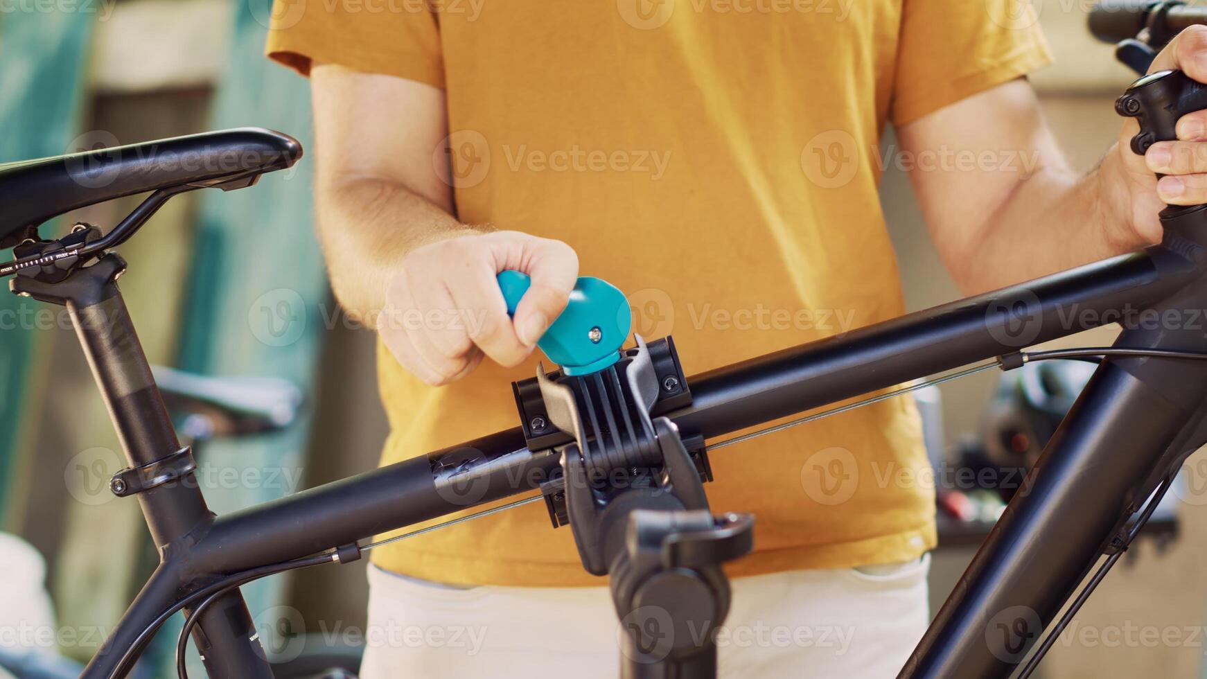 Close-up of sports-loving male grasping and securing damaged bike for adjustment on repair-stand. Caucasian person doing maintenance on bicycle while using tools in yard during summer. photo