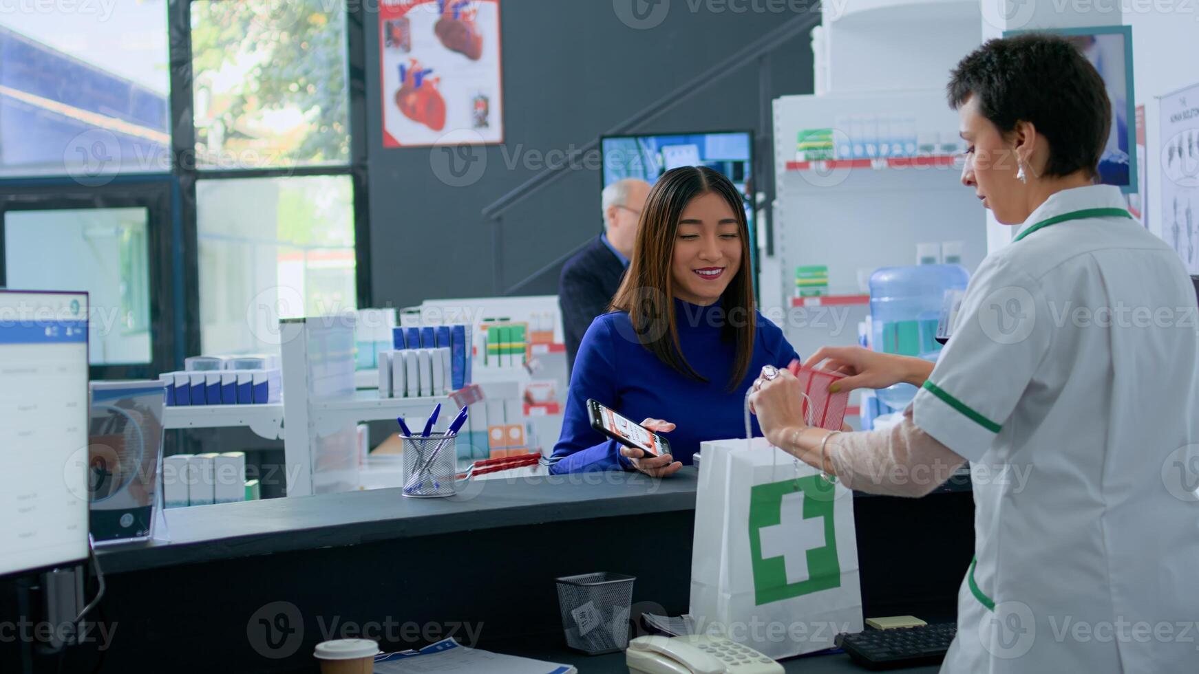 Asian customer at pharmacy counter, showing druggist prescribed heart medicine picture on smartphone, ready to purchase it. Healthcare expert selling client required medicinal product photo