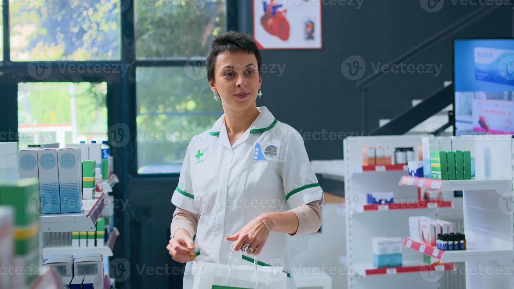 Portrait of cheerful pharmacist in apothecary preparing medicaments order for client. Smiling healthcare expert in drugstore placing cardiovascular pills in shopping bag for customer photo