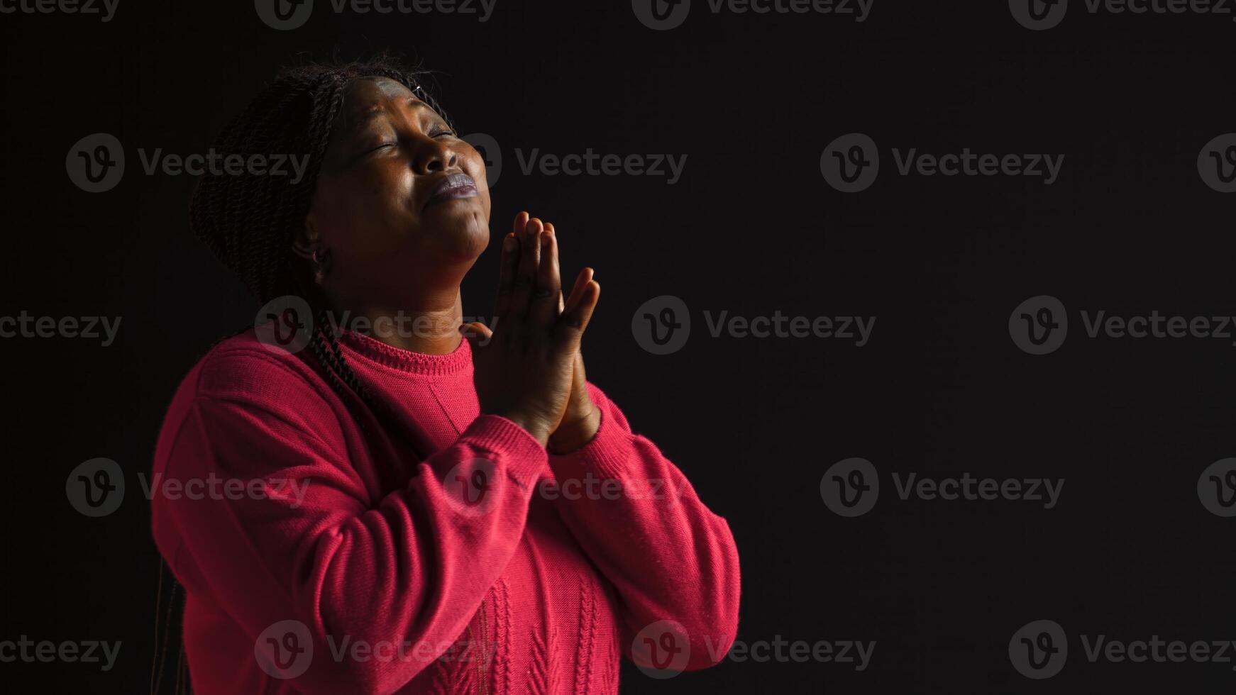 Graceful black woman gazing upwards with palms extended in gesture of reverance and adoration. Side-view portrait of african american lady engaged in prayerful reflection in isolated background. photo