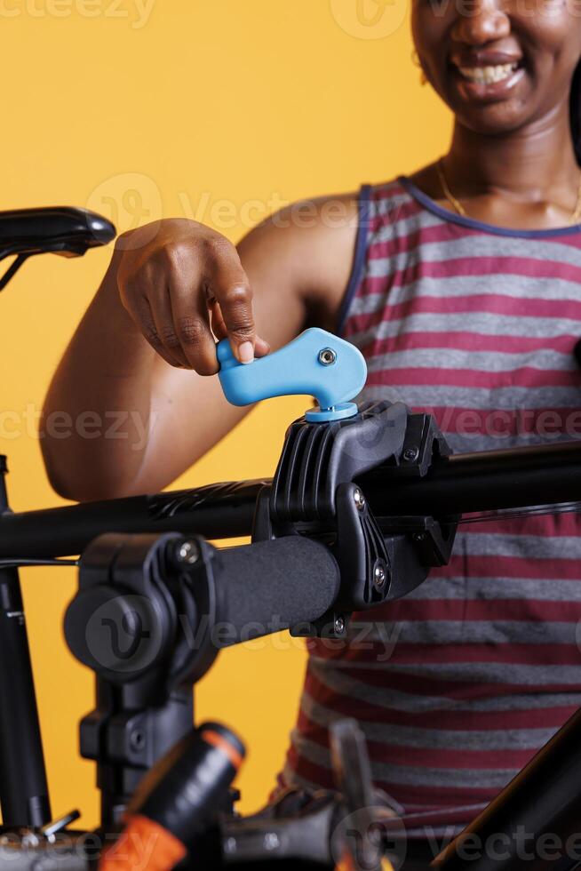 Black woman grips bicycle frame and securing it on repair stand against isolated background, showcasing dedication to cycling maintenance. Close-up of female holding the bike workstand clamp. photo