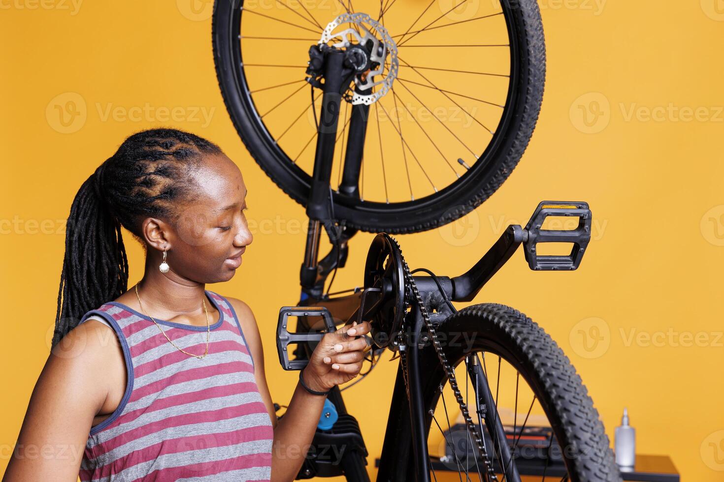 Sports-loving woman expertly adjusting broken bicycle crank arm with specialized multitool. Young african american lady carefully examining and fixing bike components with professional allen key. photo
