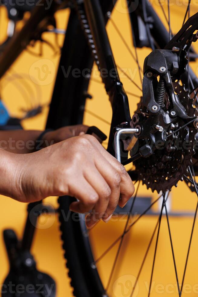 Close up of young black person adjusting bike rear derailleur with specialized equipment. Image focused on african american female hand holding an allen key to repair and maintain bicycle parts. photo