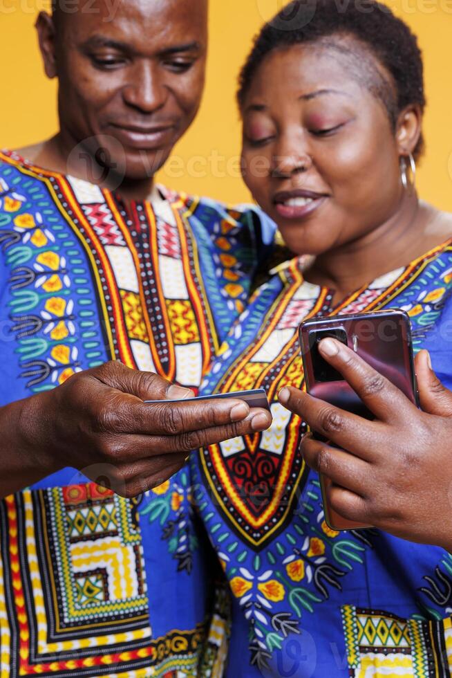 Couple holding debit card and smartphone while entering electronic banking information to pay for purchase. Black man and woman pair processing online payment on mobile website photo