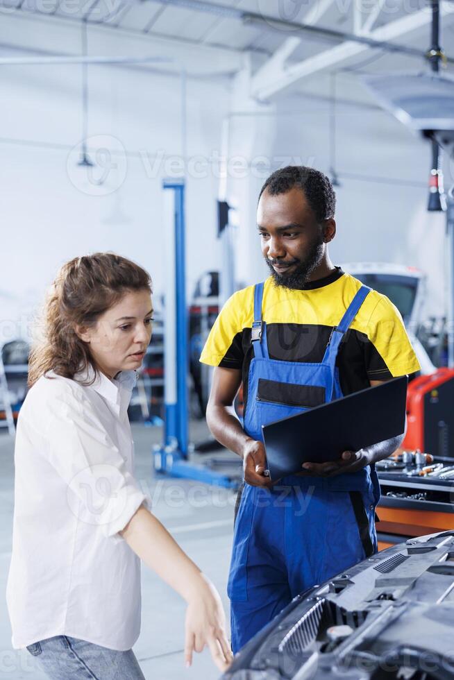 Smiling serviceman in car service uses tablet to calculate invoice after fixing broken automobile radiator. Specialist uses device to inform customer of final costs after mending vehicle photo