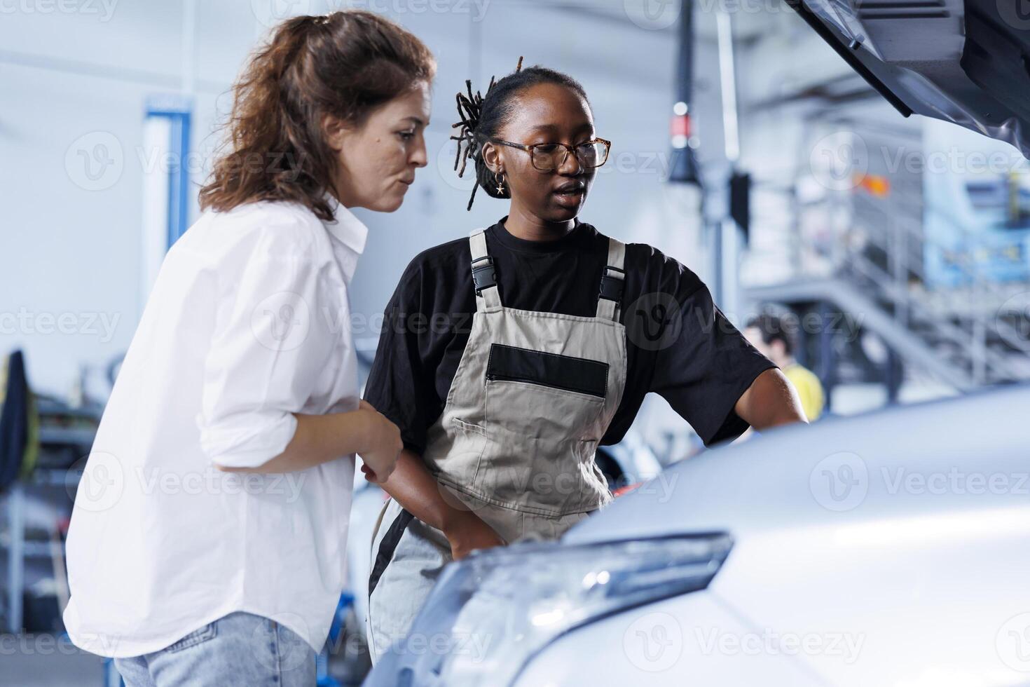Mechanic at auto repair shop conducts annual vehicle checkup, informing customer about needed compressor belt replacement. Adept garage worker talks with customer after finishing car inspection photo
