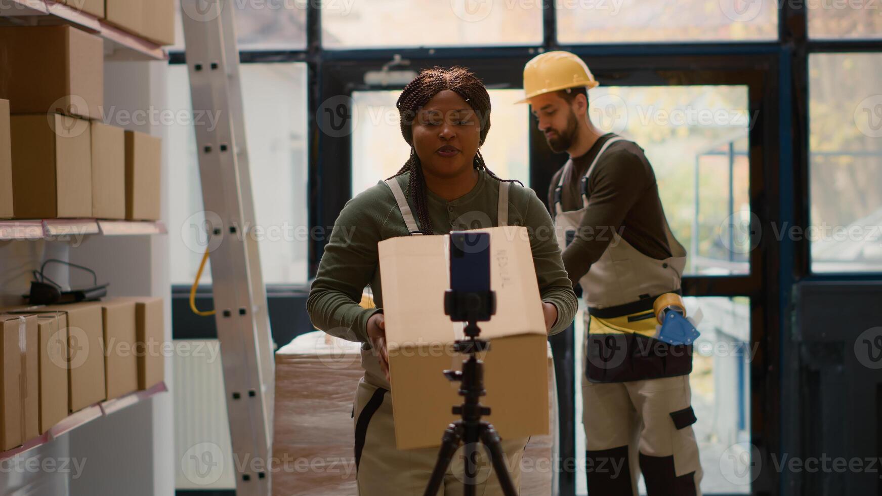 Warehouse supervisor pressing play on cellphone placed on tripod to start recording training for interns. Quality assurance manager filming tutorial showing trainees how to arrange parcels photo