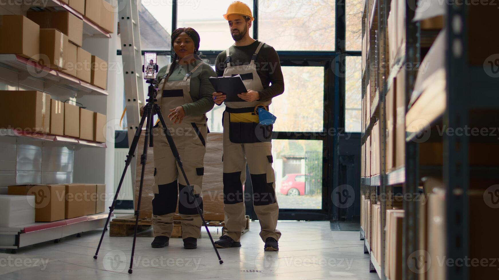 Warehouse head of operations and coworker using smartphone placed on tripod to make training for interns. Directors film themselves in fulfillment center showing trainees how to store boxes photo