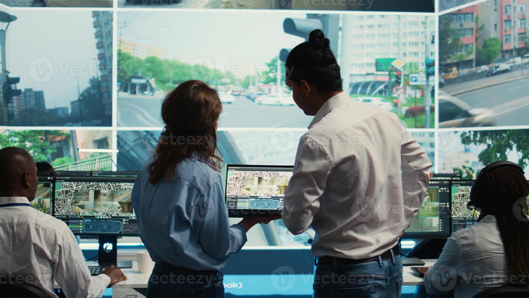 Diverse team following city traffic on a display in monitoring room, reviewing CCTV satellite radar footage. Employees working on surveillance and data collecting, control center. Camera B. photo