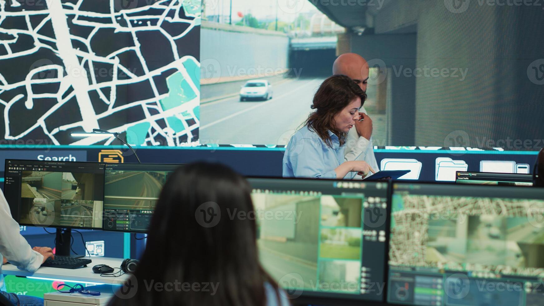 Diverse team of agency employees following delivery trucks via gps coordinates, working with CCTV surveillance footage and satellite map to ensure order shipping. Monitoring room. Camera A. photo