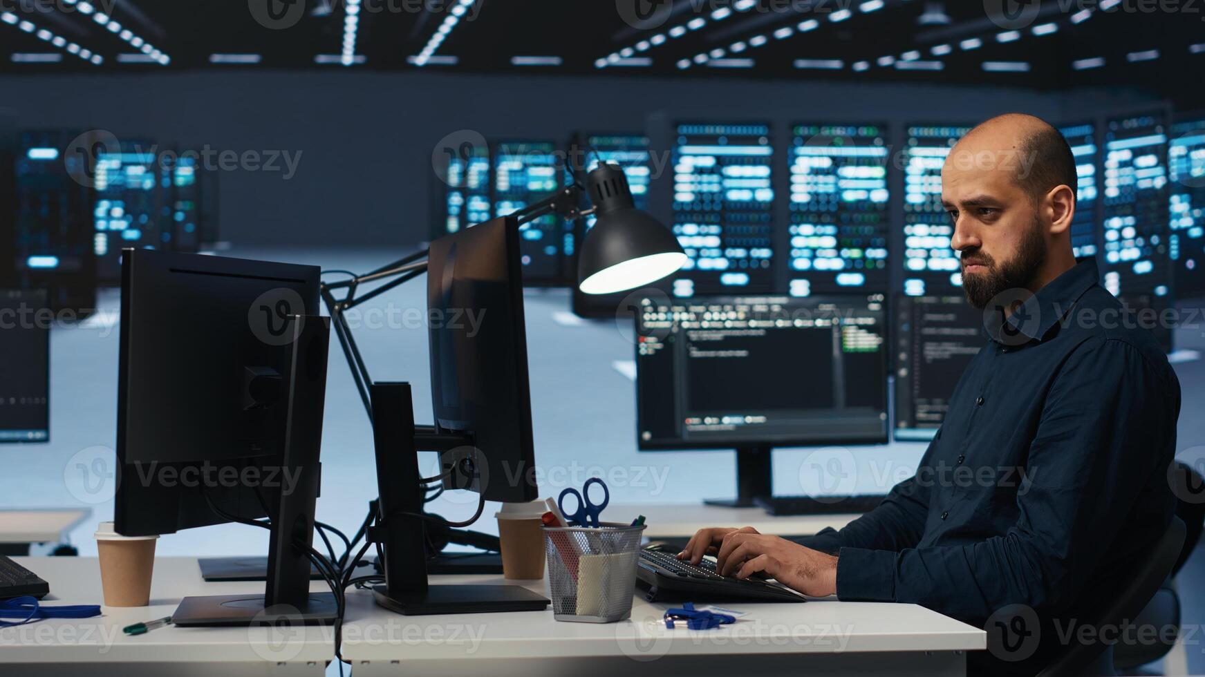 System admin focused on programming in server farm housing advanced equipment storing massive datasets. Developer typing code on PC to mend data center racks doing complex computational operations photo