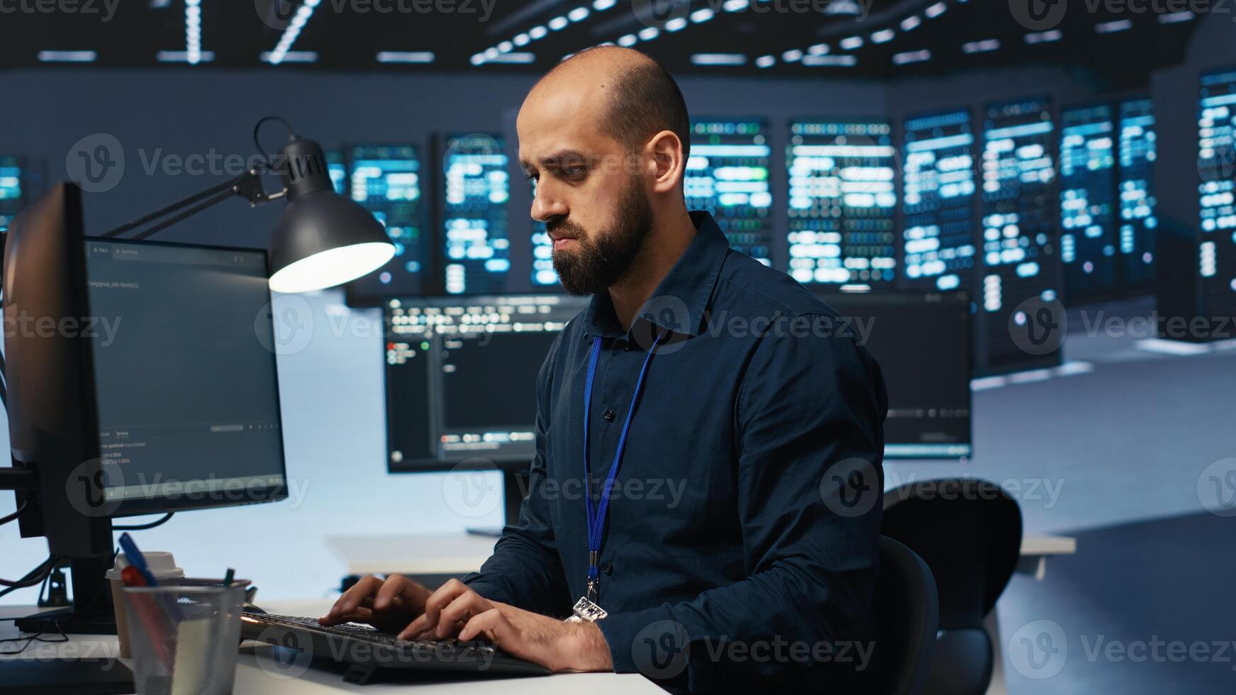 Engineer coding, working in network security data center facility hosting supercomputers, ensuring optimal performance. IT expert using desktop PC to monitor energy consumption across server cabinets photo