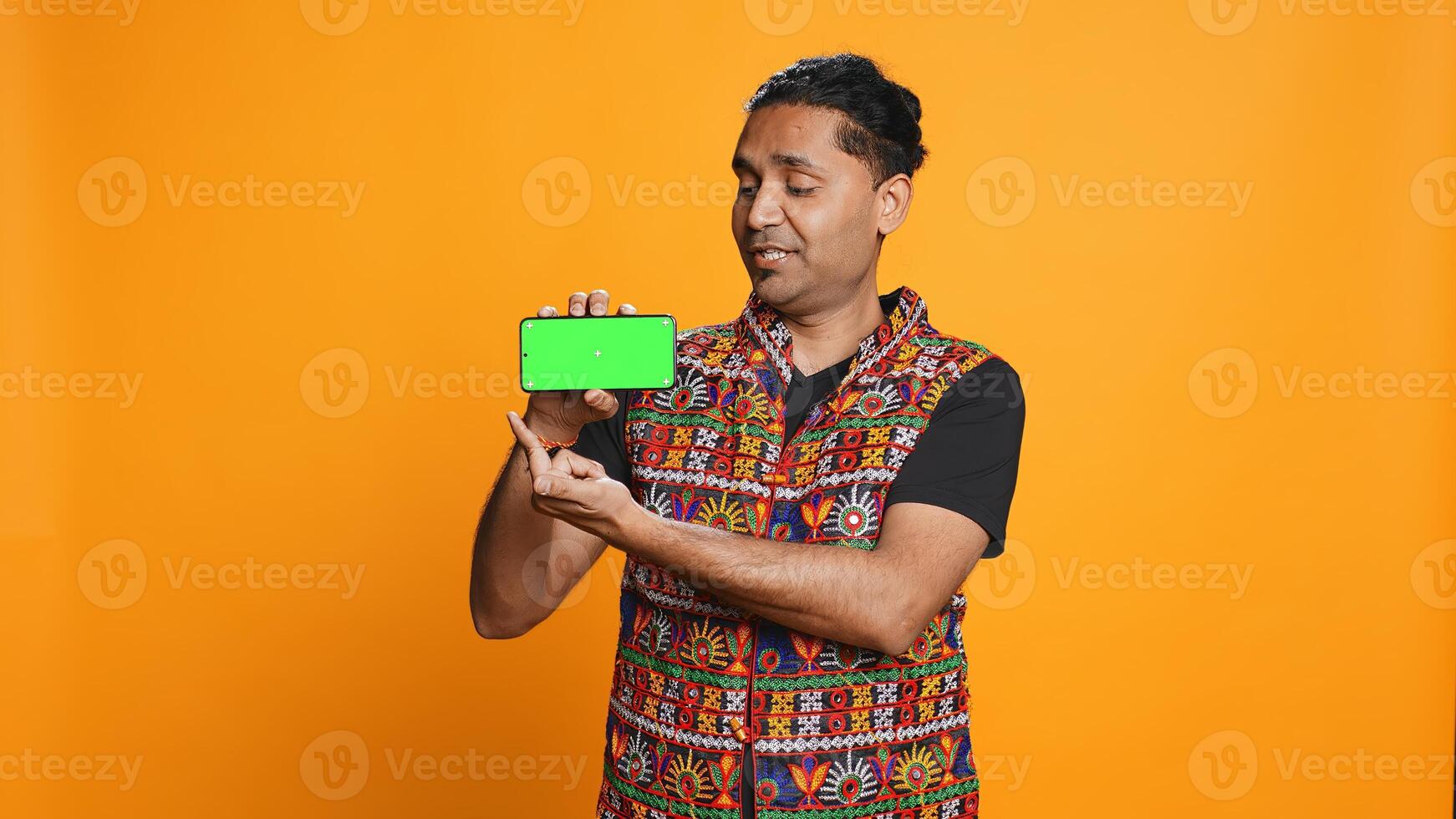 Content creator in traditional clothing recommending isolated screen phone, studio backdrop. Indian man reviewing copy space mockup smartphone device for online tech channel, camera B photo