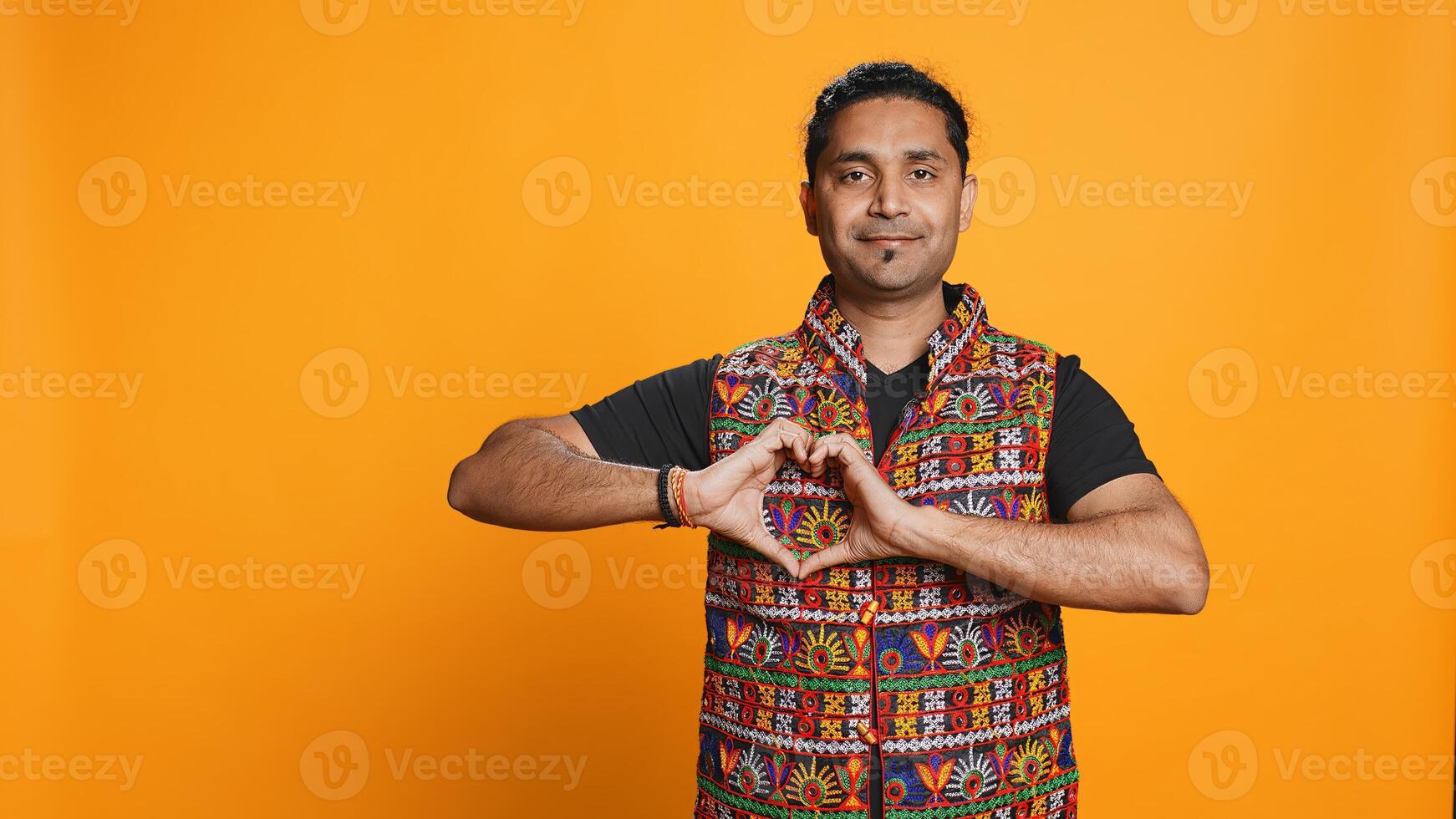 Portrait of jolly friendly indian man doing heart symbol shape gesture with hands. Cheerful nurturing person showing love gesturing, isolated over studio background, camera B photo