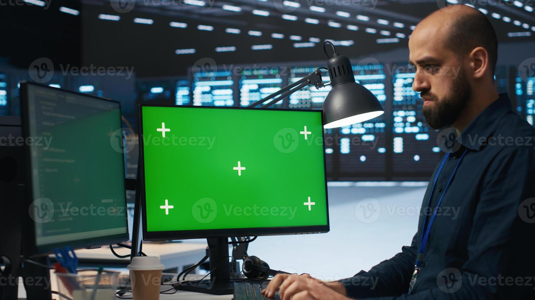 System administrator working on green screen computers in data center, ensuring optimal performance. Worker monitoring energy consumption across servers with mockup PC displays photo