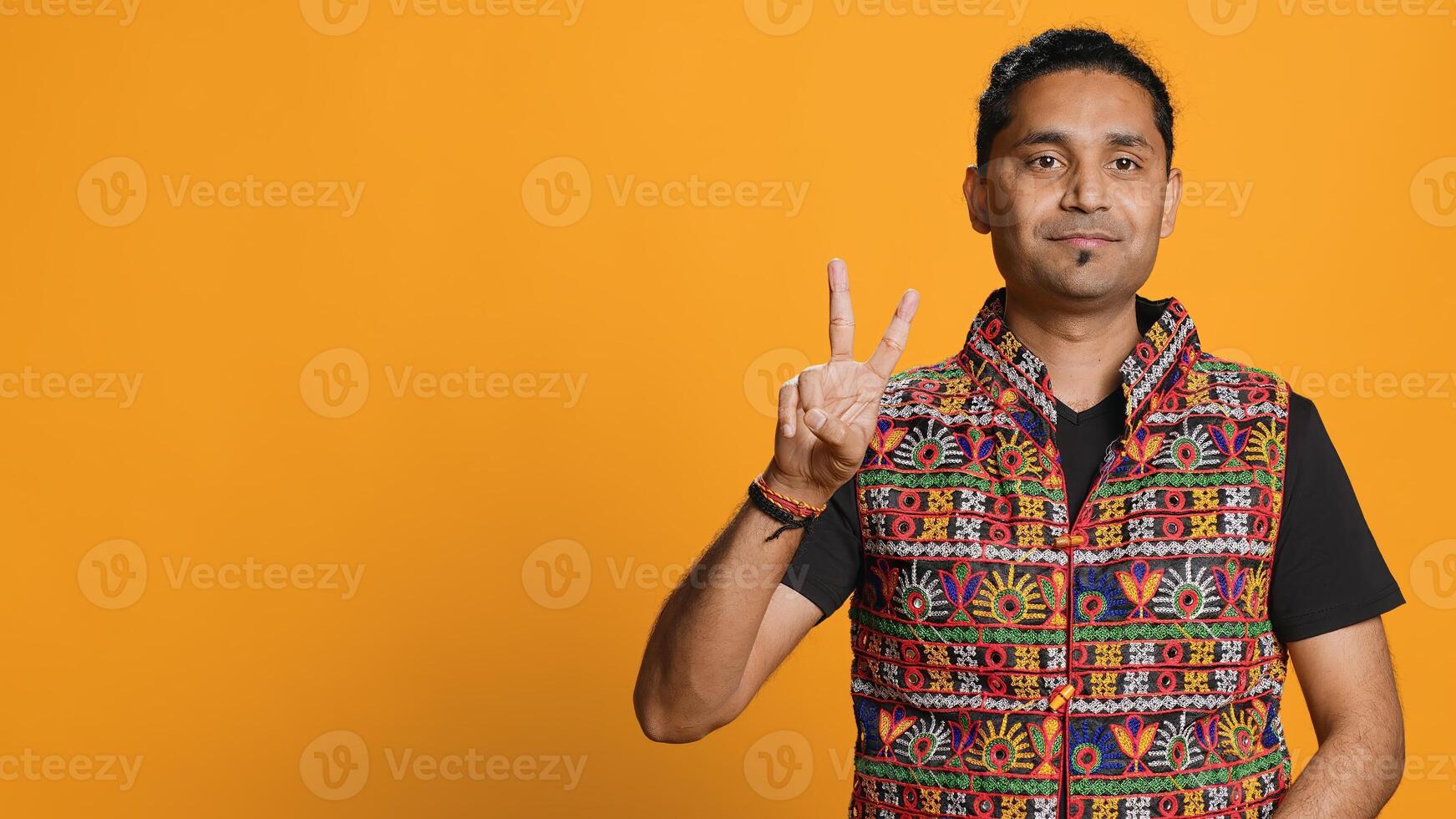 Portrait of upbeat man crossing fingers to make wish, hoping for good luck, isolated over studio background. Jolly indian person doing peace victory hand sign gesture, camera A photo
