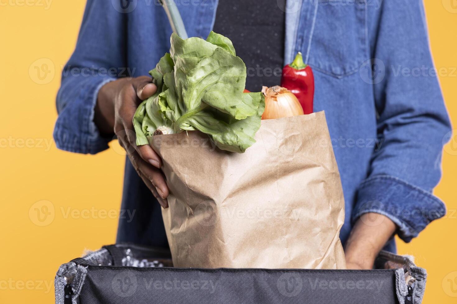Male model courier emptying a paper bag full of fresh groceries, using backpack to bring local farmers market orders to clients. African american guy working in takeout industry. Close up. photo
