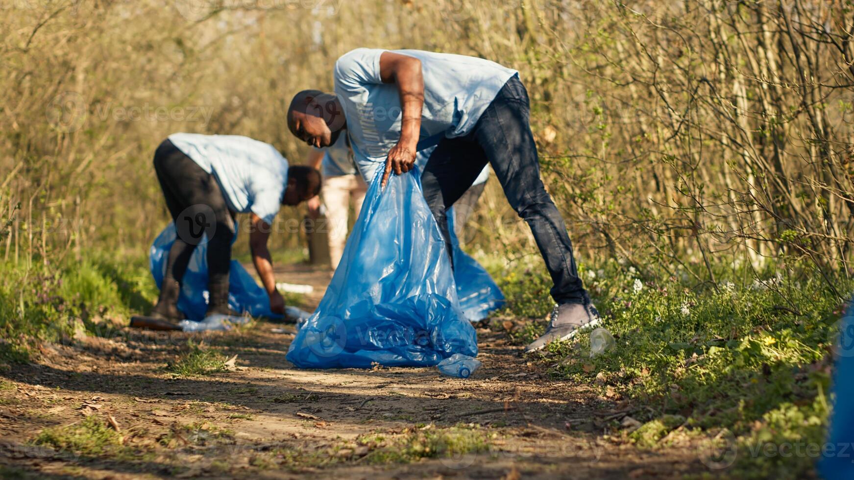 People picking up trash and plastic bottles from the forest area, protecting the natural environment and doing voluntary work. Activists group cleaning the woods, recycling waste. Camera A. photo
