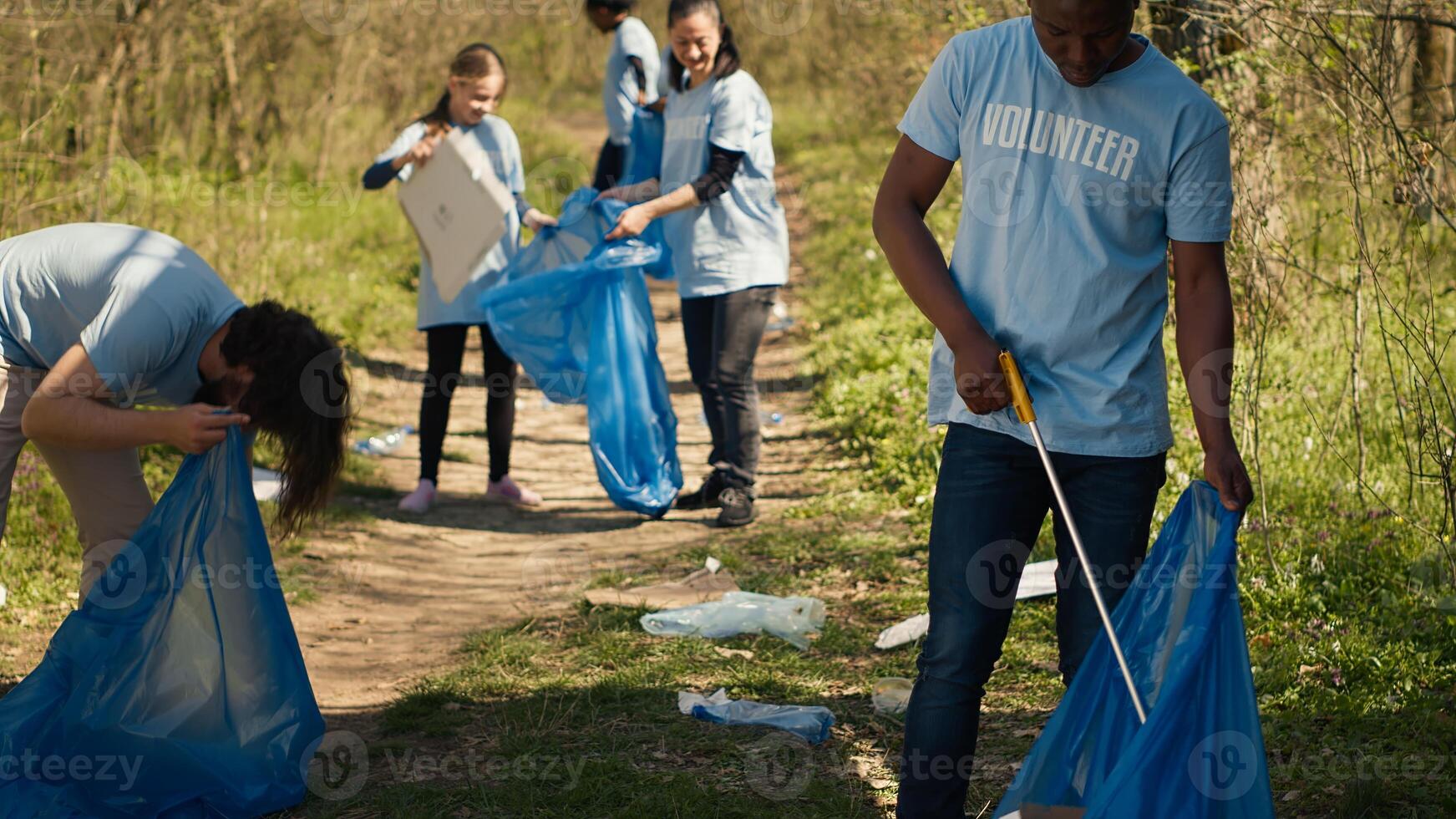 Eco friendly activist grabbing garbage and plastic waste from a forest area, cleaning up the woods and collecting rubbish in a trash bag. Man volunteer dealing with waste management. Camera A. photo