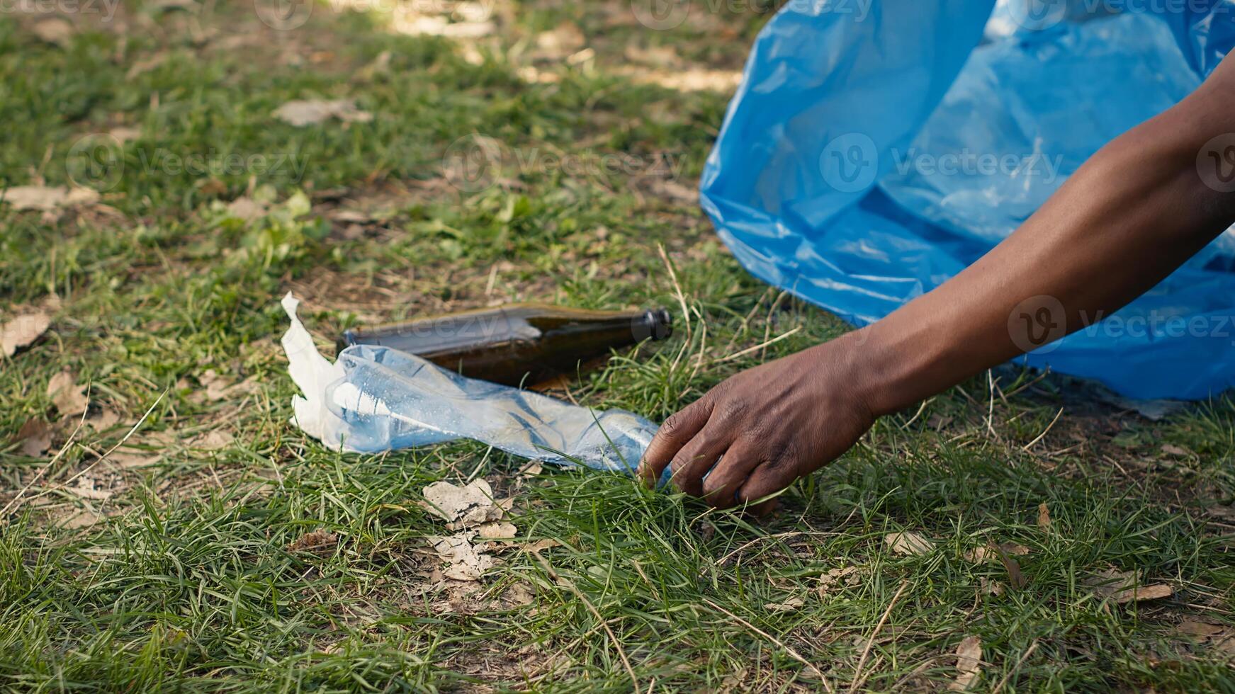 People supporting cleanup of the natural environment by grabbing recyclables and trash objects from the woods, collecting in a garbage bag. Using utensils to pick up rubbish. Close up. Camera A. photo