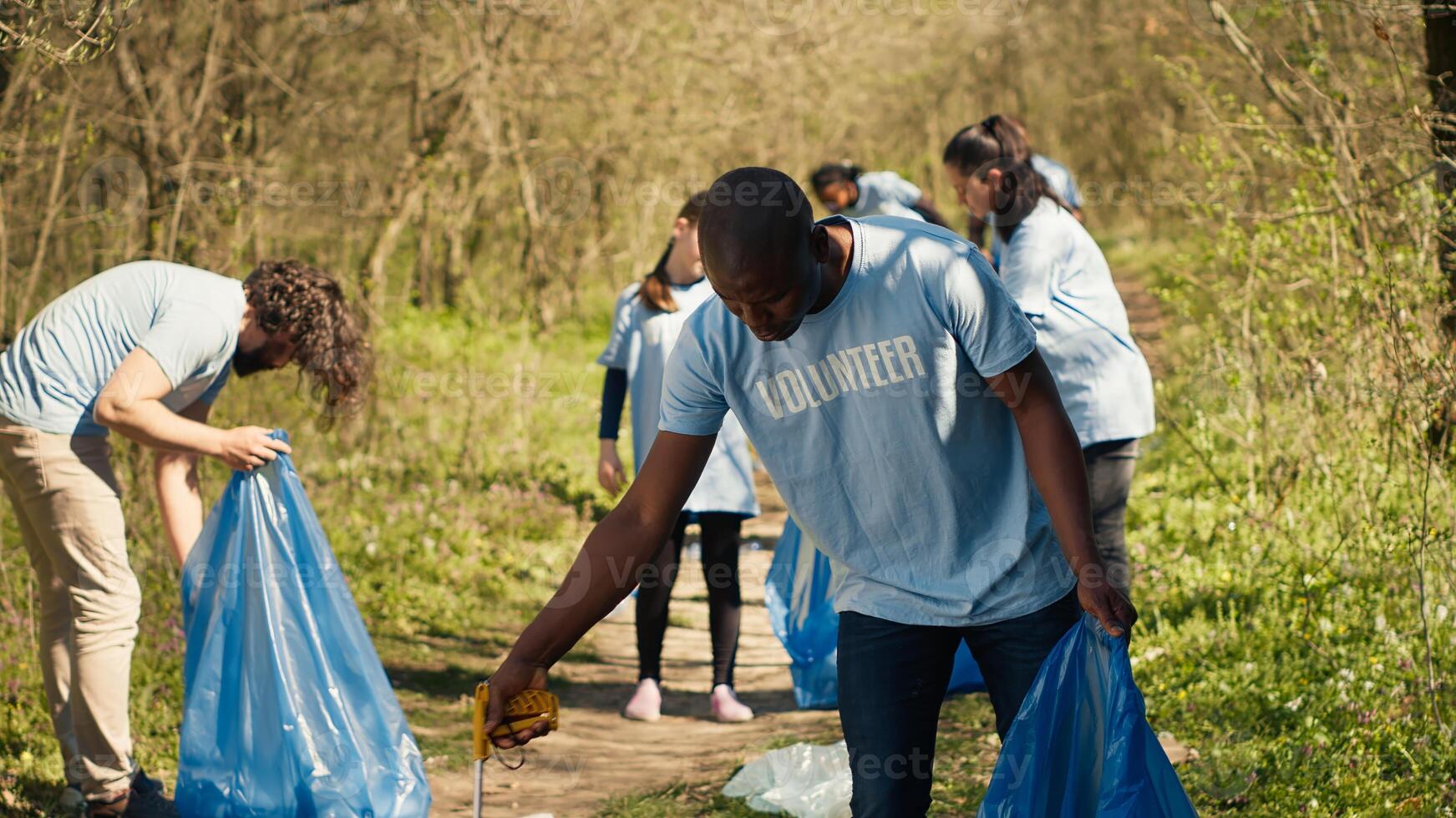 African american man volunteer collecting trash and plastic waste with tongs, grabbing rubbish and recycling in a garbage disposal. Activist combating forest pollution and illegal dumping. Camera A. photo