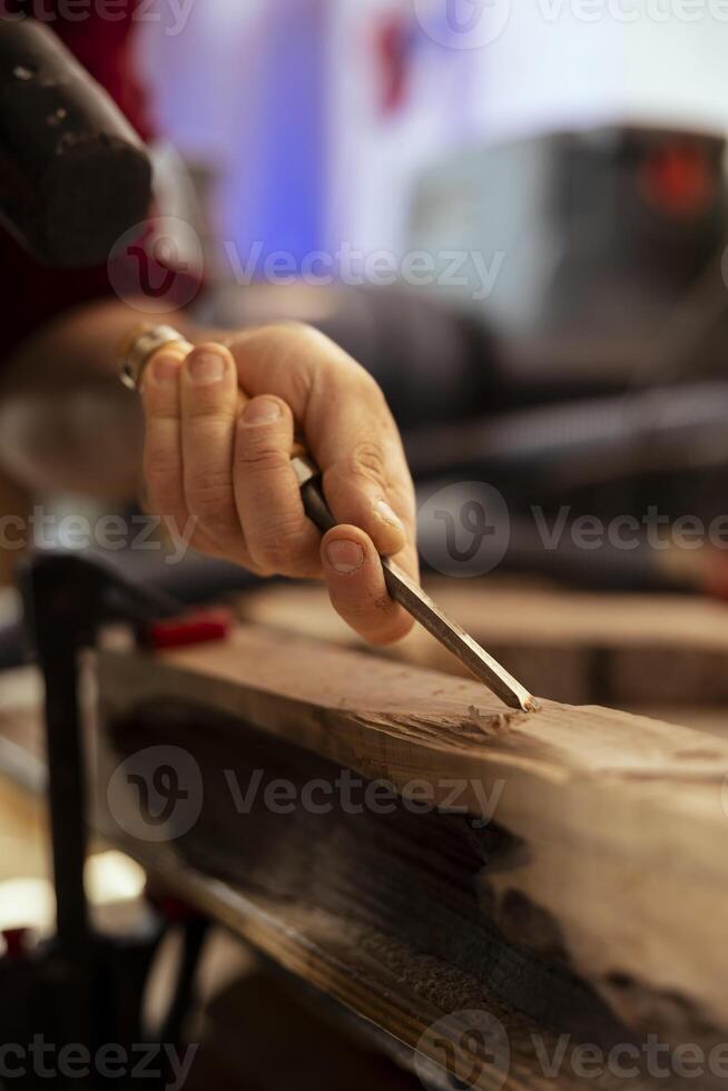 Manufacturer meticulously carving intricate designs into wood using chisel and hammer in carpentry shop. Carpenter in woodworking workshop shaping wooden pieces with tools, close up shot photo